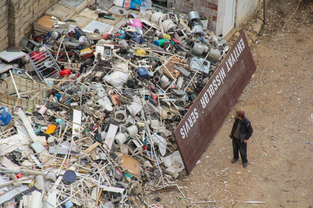 A person inspecting a large pile of scrap metal and electronic waste in an outdoor junkyard